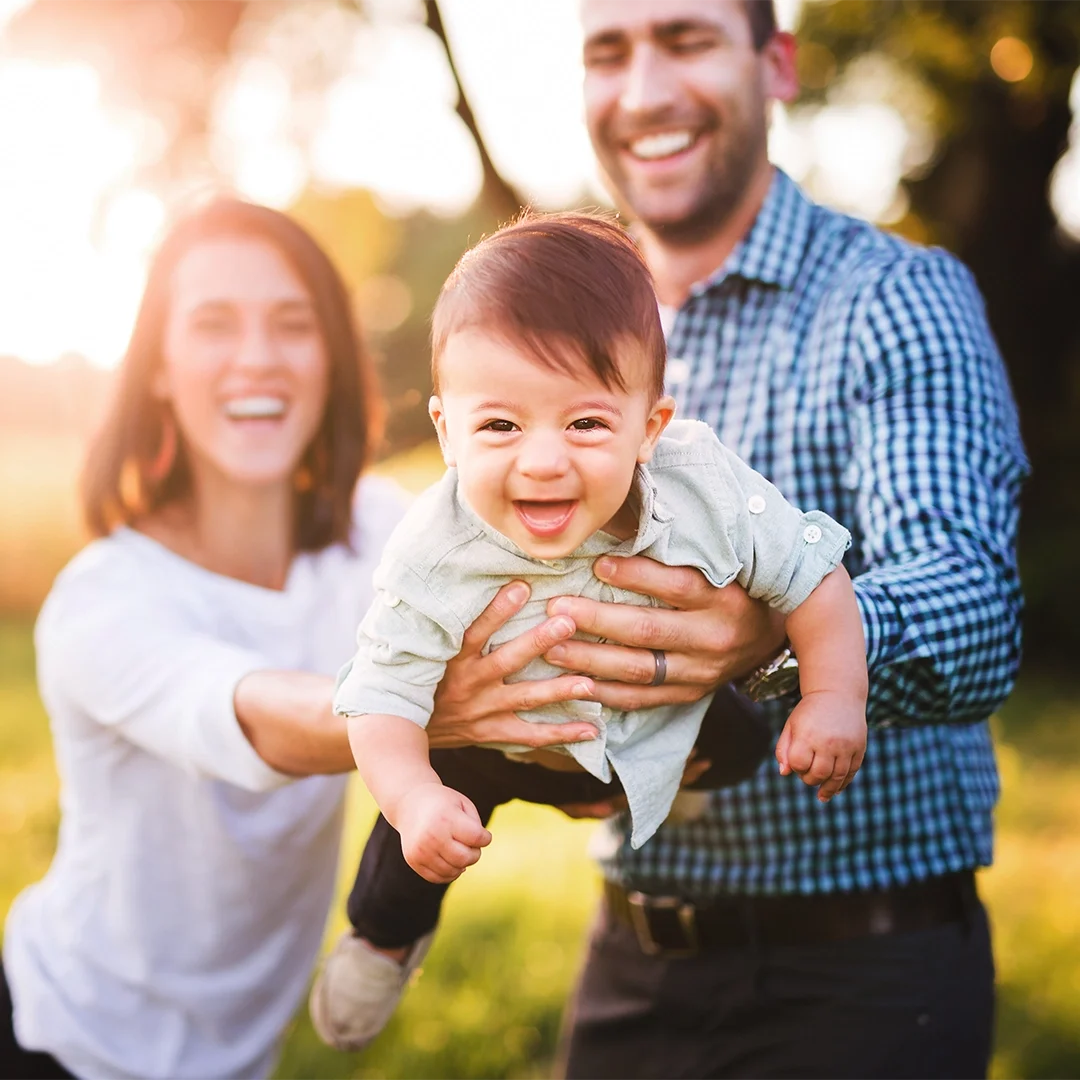 Happy parents and baby smiling outdoors representing caring family dentistry services